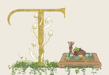 Gold letter T with vines on a floor of green leaves and vines and a wooden table with tea accessories on top